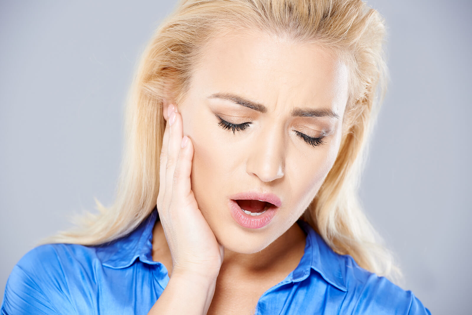 Beautiful young blond woman suffering from toothache holding her